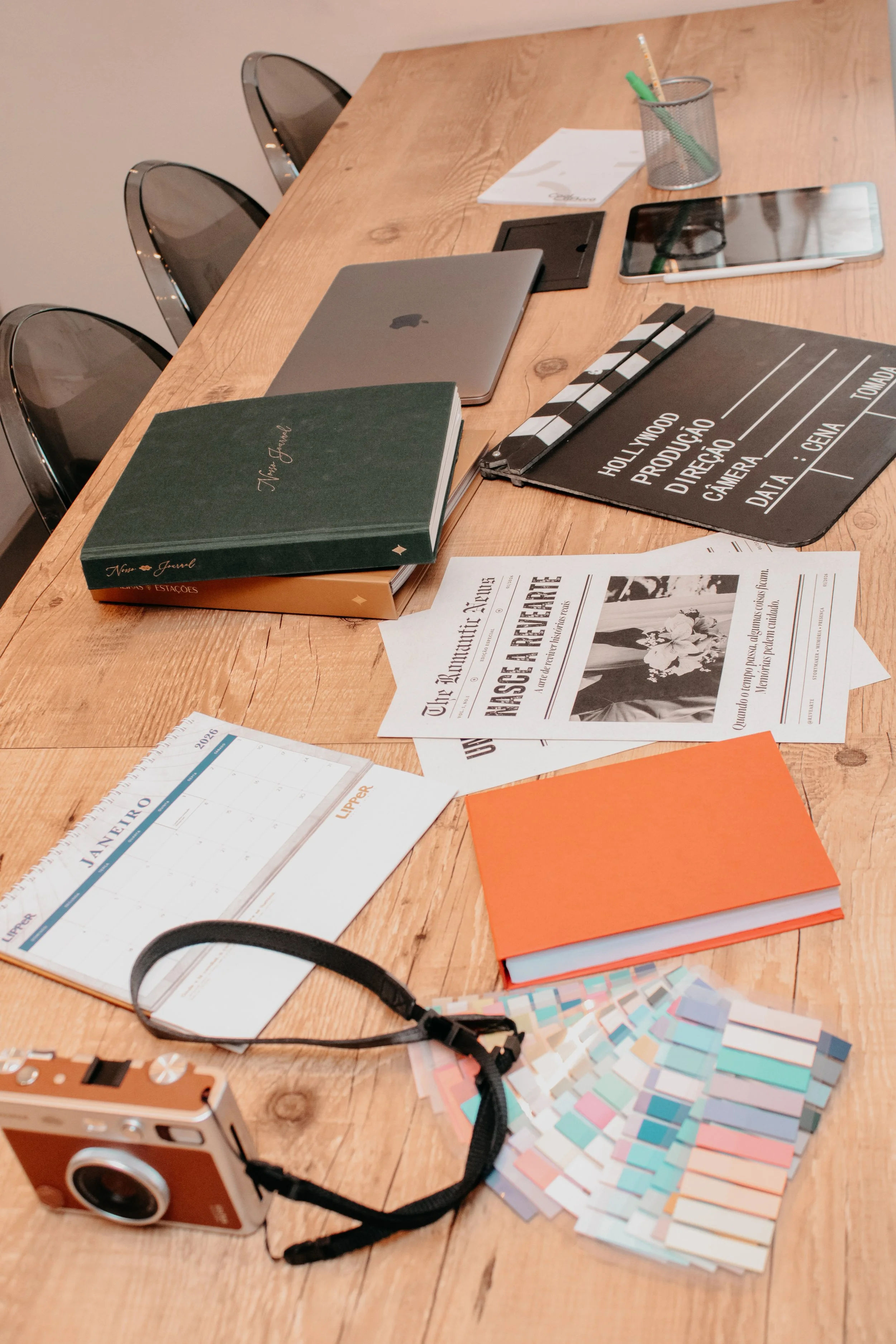 Mesa de trabalho com acessórios de fotografia, design e cinema, destacando jornais vintage, câmera analógica e ferramentas de organização para 2026.