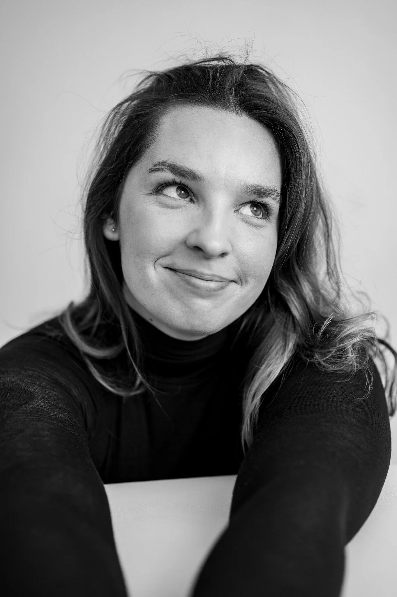 A woman with shoulder-length hair, wearing a black turtleneck, smiling slightly, looking upward, in a black-and-white portrait.