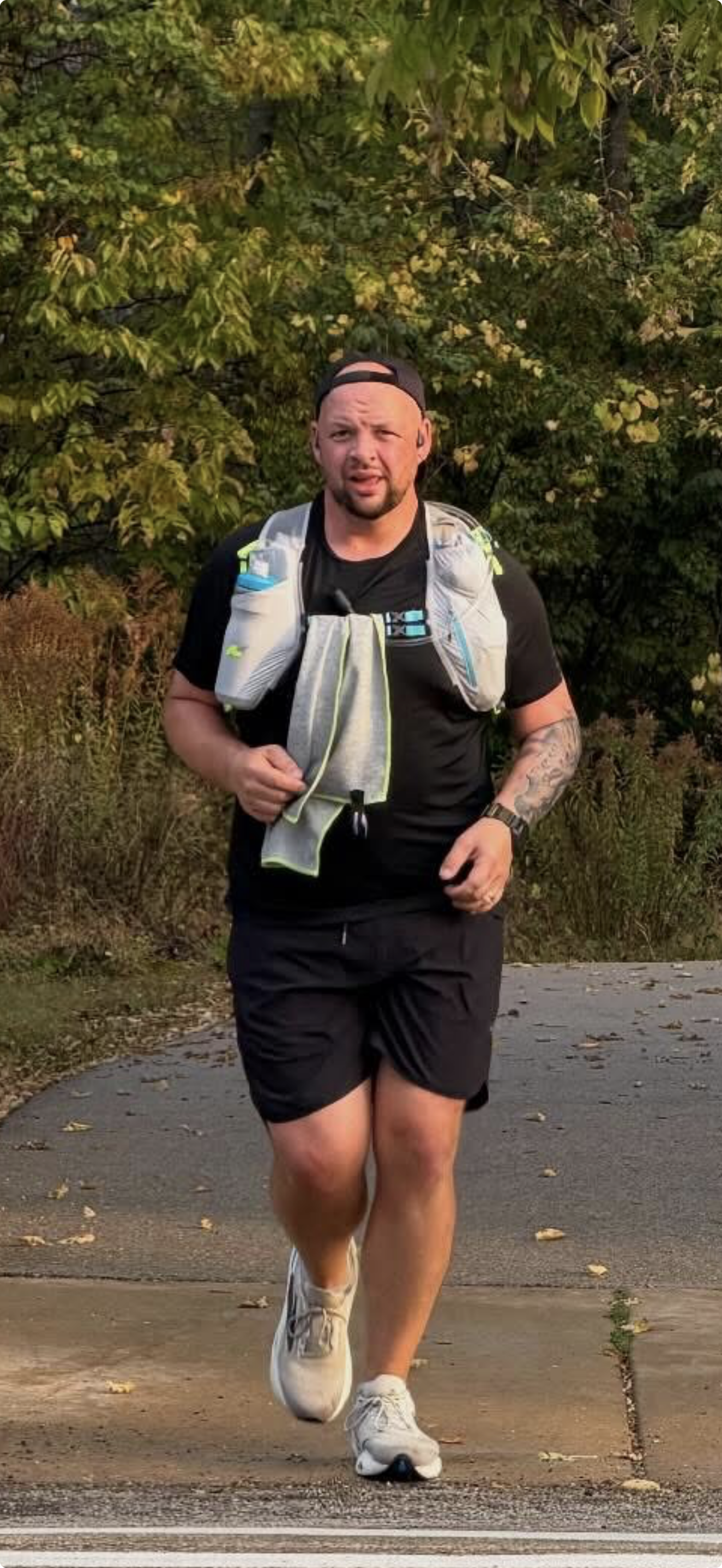 A man in athletic clothing running outdoors on a paved path with trees in the background.