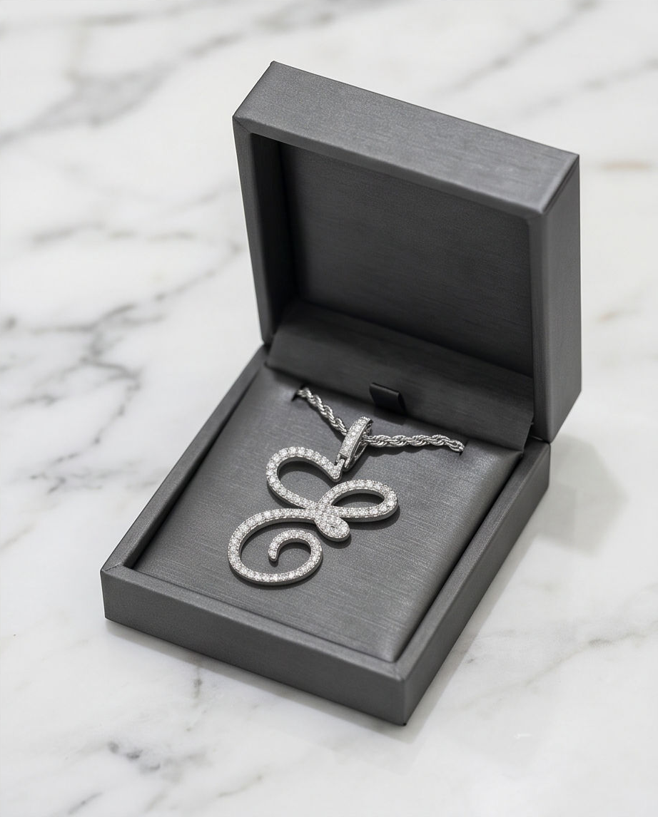 A silver necklace with an intricate pendant resting in a black jewelry box on a white marble surface.