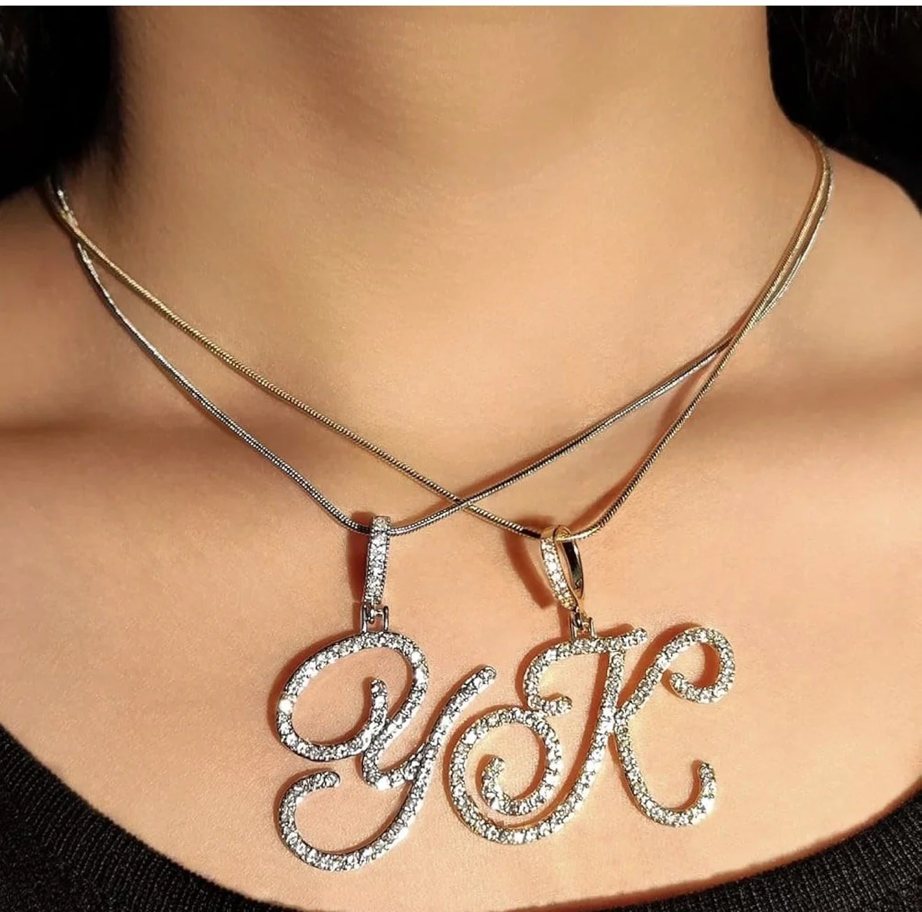 Close-up of a woman's neck and collarbone with three layered necklaces, including one with a 'Love' pendant, all adorned with sparkling gemstones.