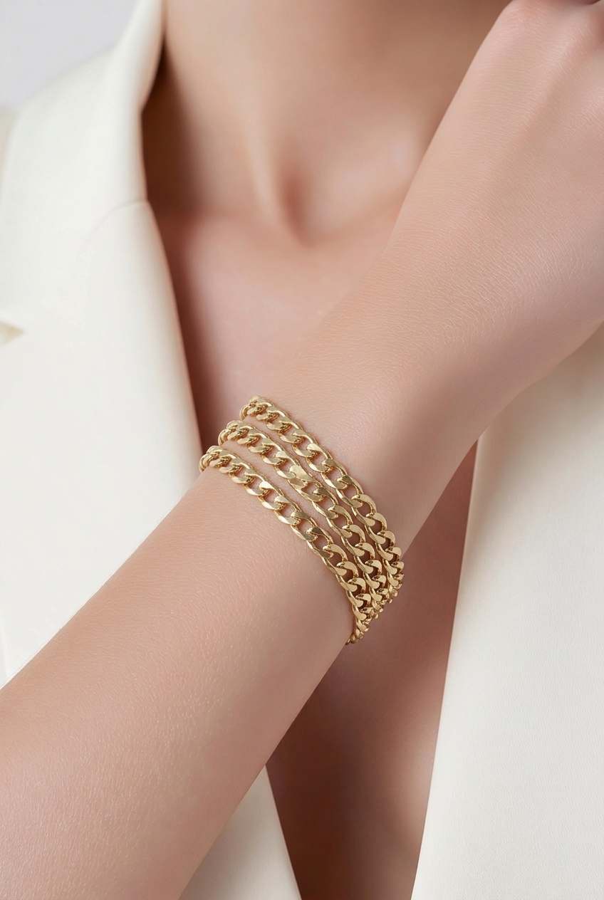 Close-up of a woman's wrist wearing layered gold chain bracelets, with part of her hand and neck visible, dressed in a white shirt.