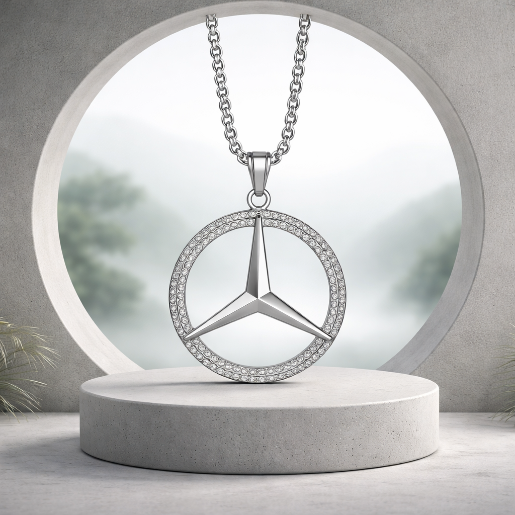 A silver Mercedes-Benz logo necklace with embedded rhinestones, hanging from a chain and displayed against a blurred outdoor background.