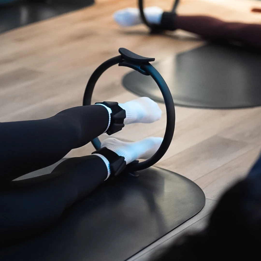 A person wearing black clothing and white gloves is seen holding a black circular object with a strap, possibly a VR headset, on a wooden table.