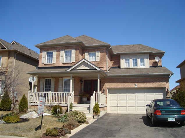 A two-story brick house with a front porch, a driveway, and a car parked outside on a clear day.