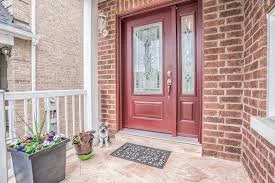 Red front door with glass panels, brick exterior, and a welcome mat. Potted plants with flowers are near the entrance.