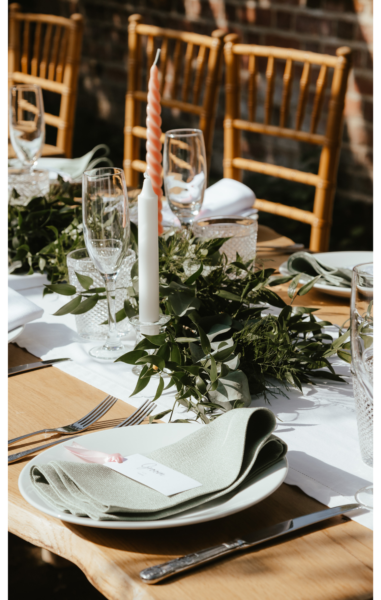 Elegant outdoor dining table with a floral centerpiece, candles, glassware, and place settings with napkins and name cards.