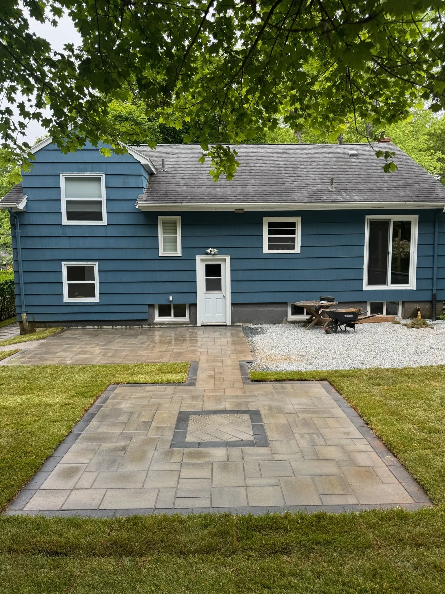 Front view of a blue house with multiple windows, a white door, and a paved patio area with grass on either side.