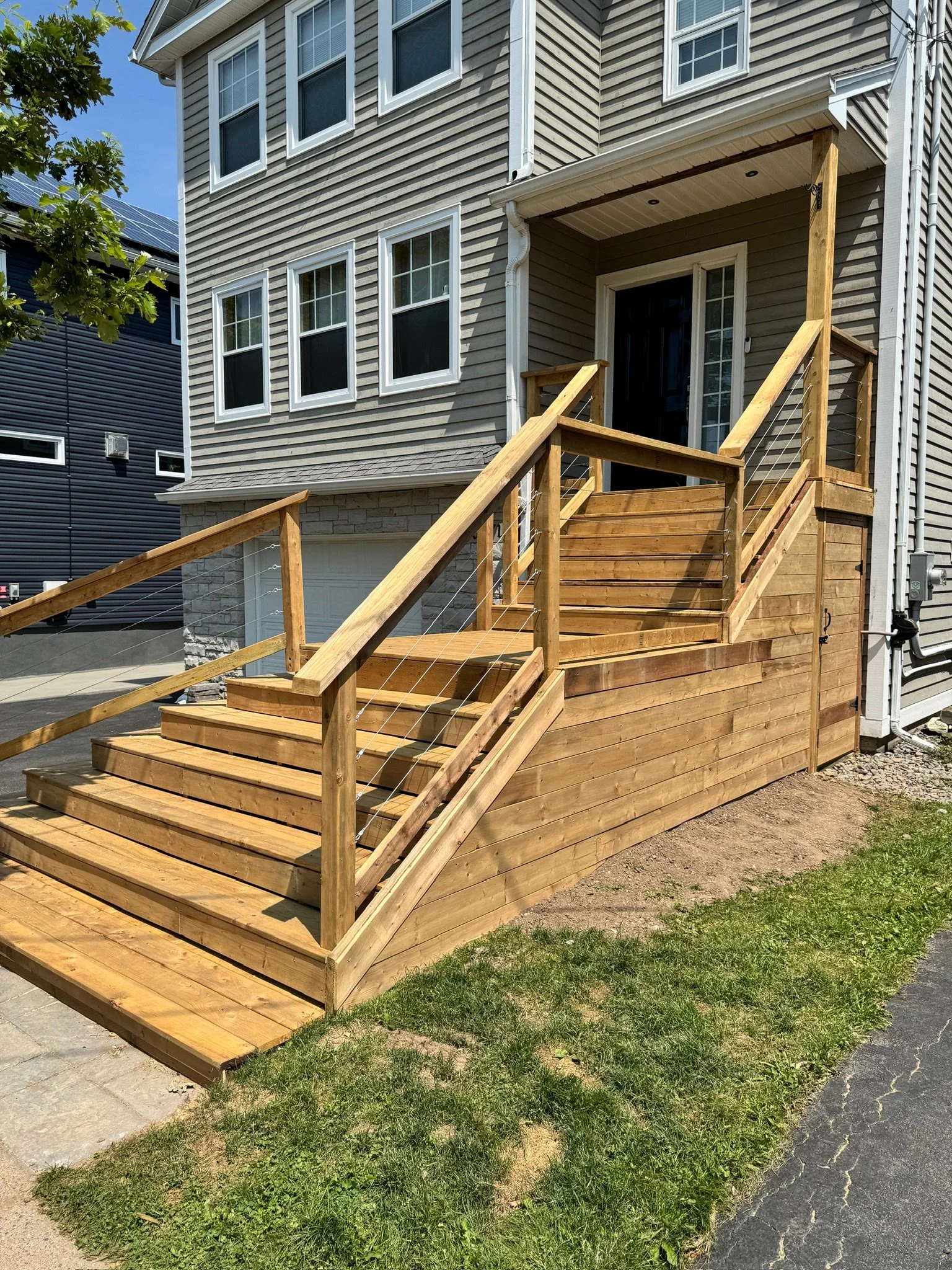 New wooden stairs and porch built outside a house with siding, leading up to the front door.
