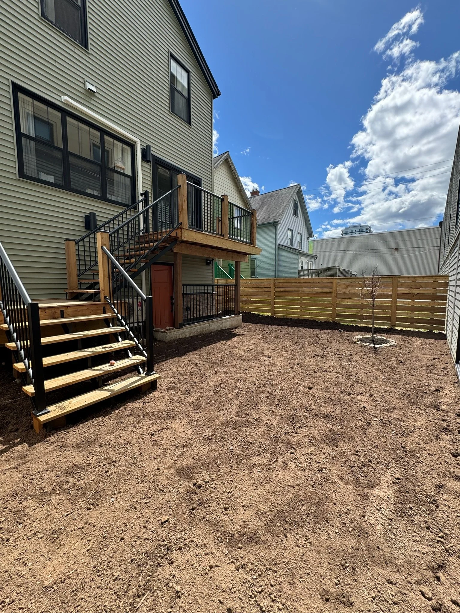Backyard with newly built wooden deck and stairs, small tree, and vinyl fencing, under partly cloudy sky.