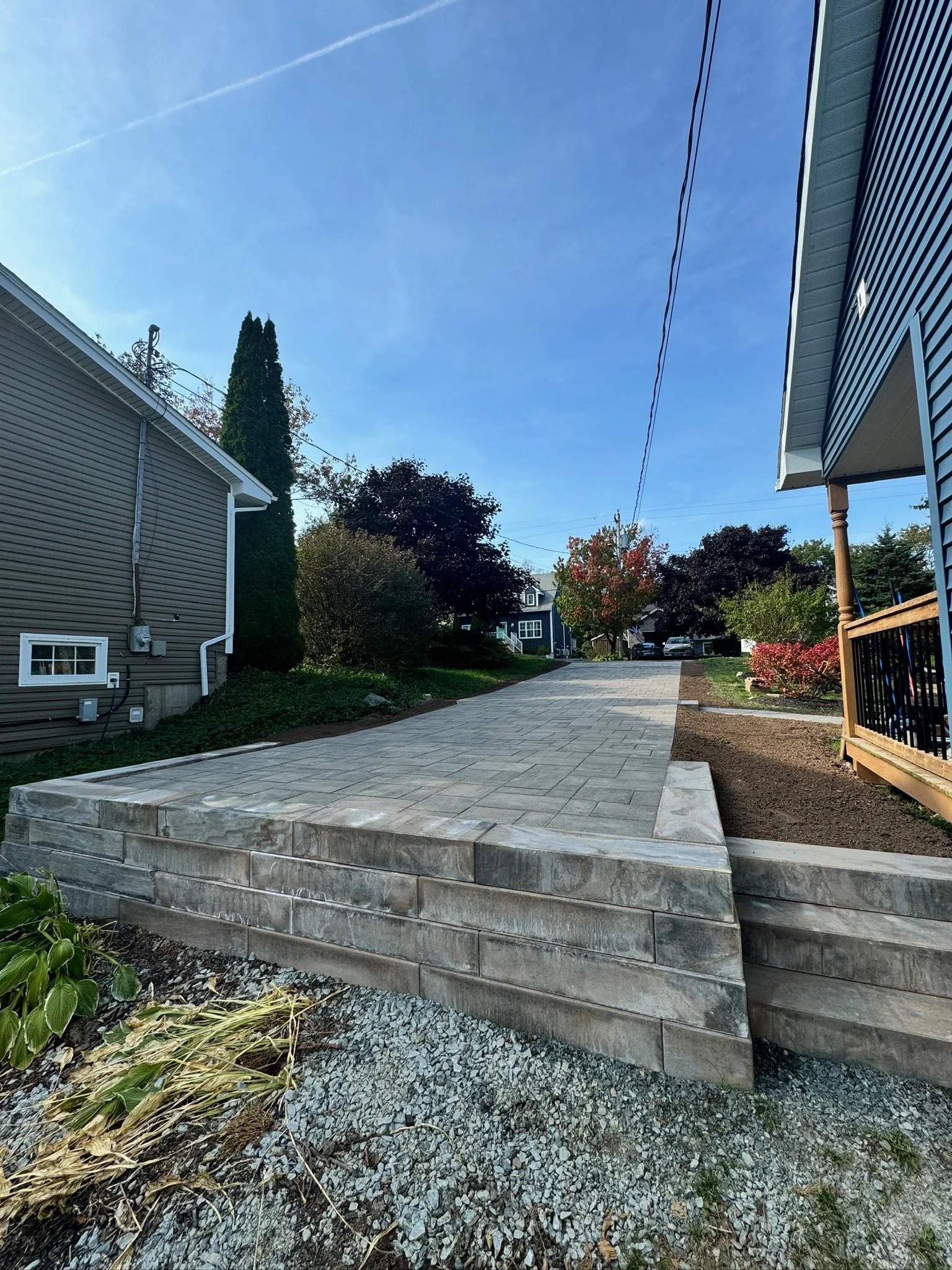 New concrete driveway with steps leading to a house, surrounded by lawns and trees, under a clear blue sky.