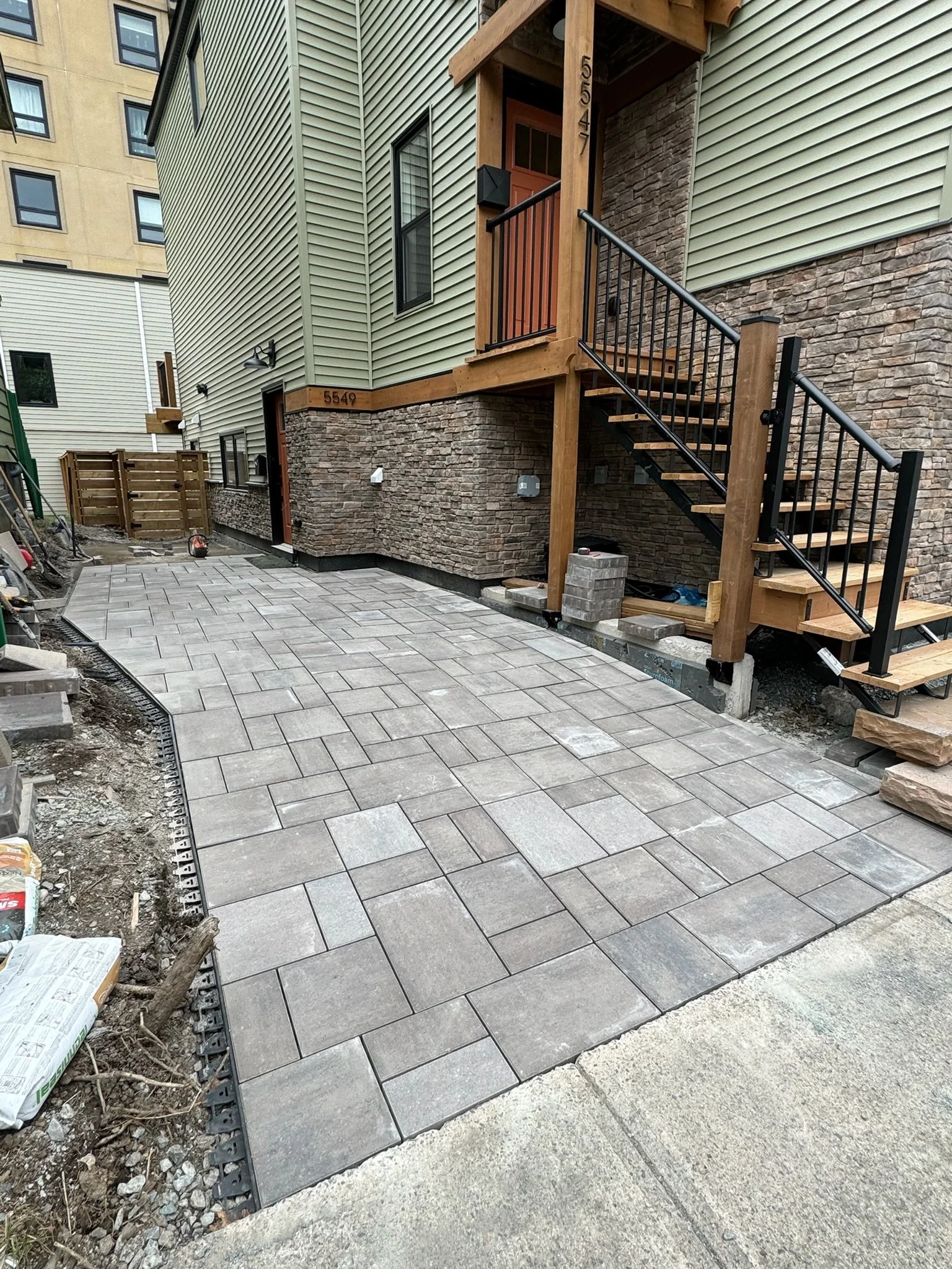 Newly paved stone driveway leading to the entrance of a residential building with stairs, with construction materials and tools around.