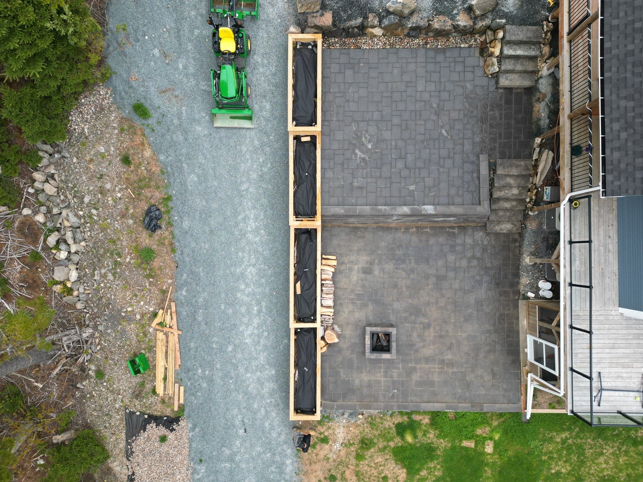 Aerial view of a construction site with materials, two green tractors, and a partly finished patio area with stones and wood framing.