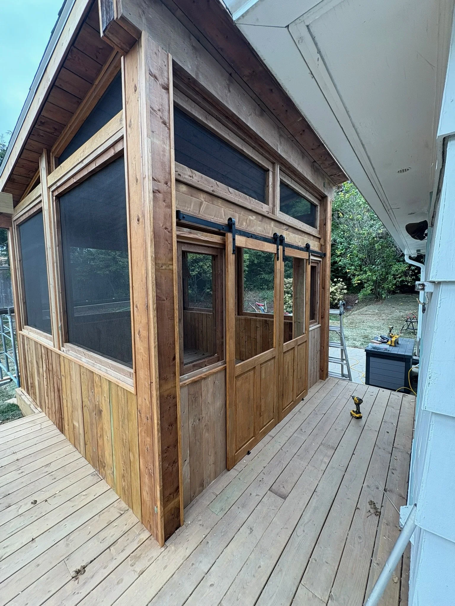 A wooden screened porch or sunroom under construction attached to a house with tools nearby.