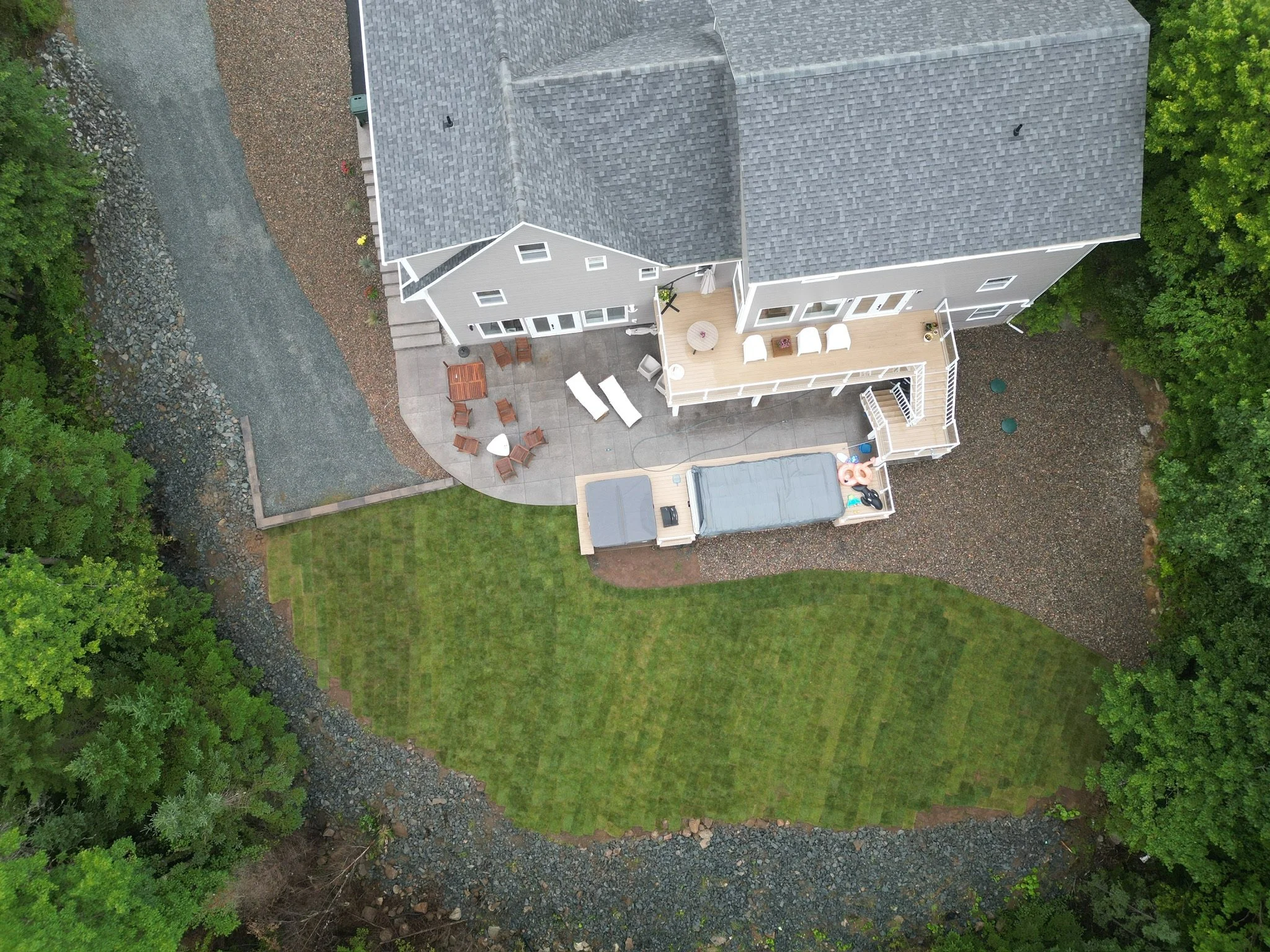 Aerial view of a backyard with a house, patio area, lawn, and surrounding trees.