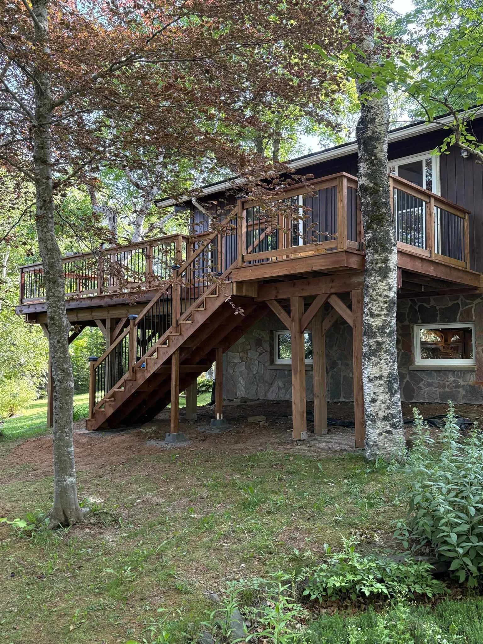A wooden deck with stairs attached to a house, surrounded by trees and greenery in a backyard.