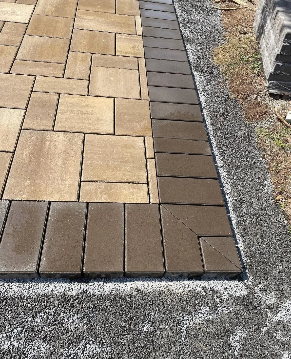 Close-up view of a newly paved sidewalk with concrete pavers, bordered by gravel and construction materials.