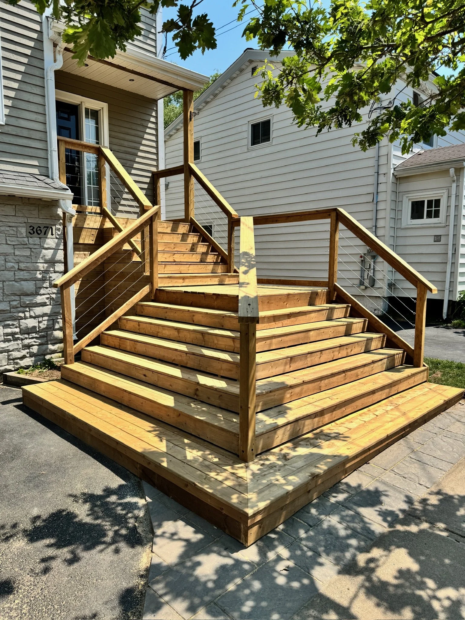 New wooden staircase with railings outside a house, casting shadows on the walkway.