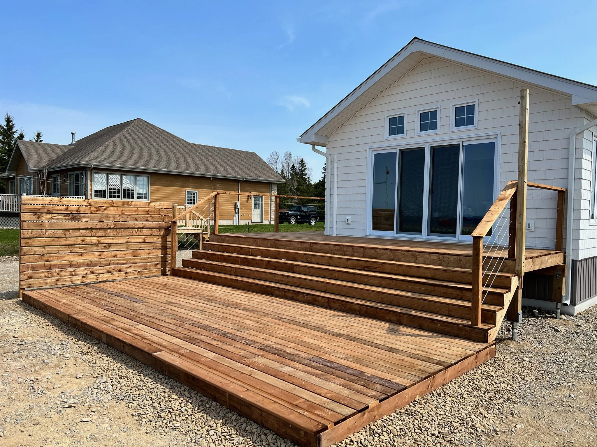 New wooden deck with stairs and railing attached to a white house with sliding glass doors, under a blue sky.