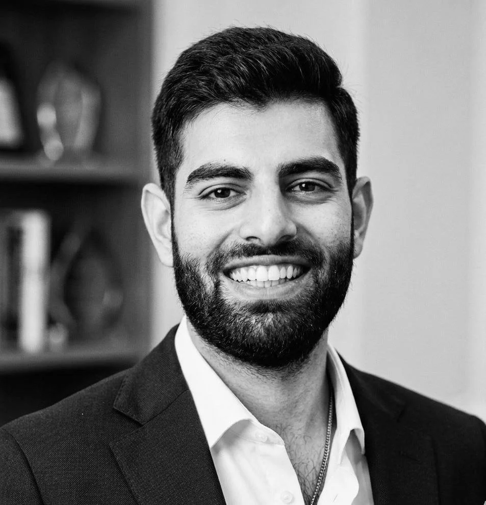 Black-and-white photo of a smiling man in a suit with a beard and short dark hair.