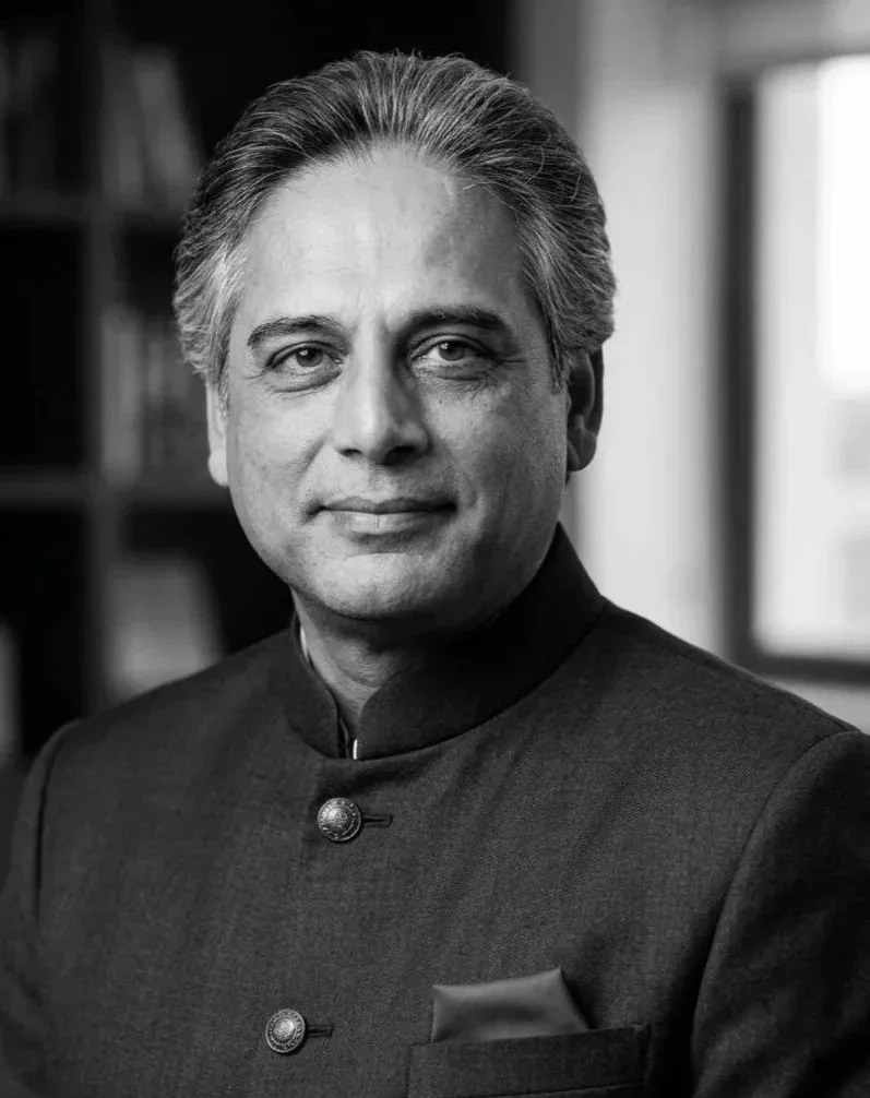 Black and white portrait of a man wearing traditional Indian attire, with a Nehru collar, standing indoors with bookshelves in the background.