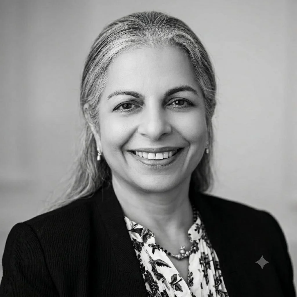 Black-and-white professional portrait of a smiling woman with shoulder-length gray hair, wearing a dark blazer, patterned blouse, necklace, and earrings.
