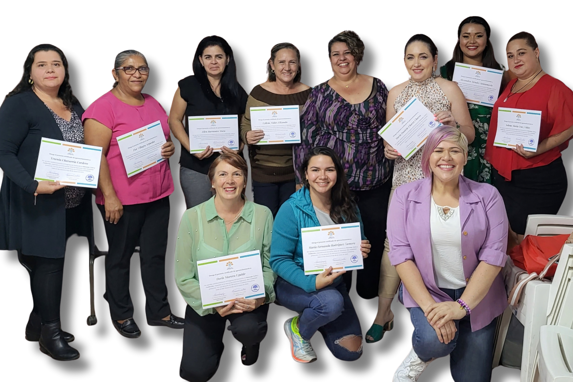 Group of women holding certificates, posing for a photo, standing and sitting against a black background, smiling, some wearing colorful clothing.