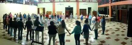 Group of people holding hands in a large indoor hall.