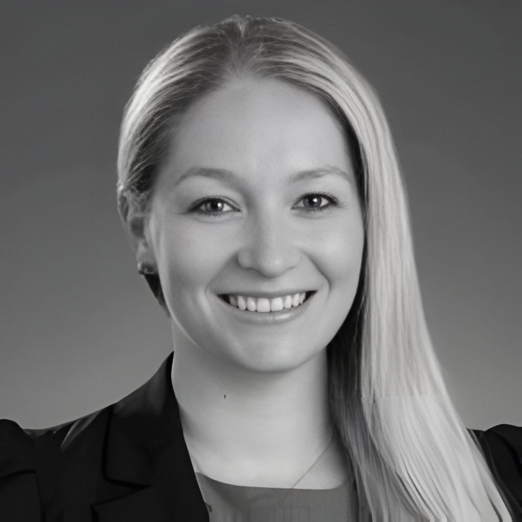 Black and white professional headshot of a smiling woman with long straight hair, wearing a blazer.
