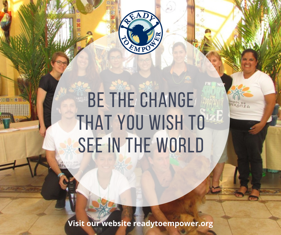 Group of people at an event with a logo reading 'Ready to Empower' and a message encouraging change, with plants and colorful decorations in the background.