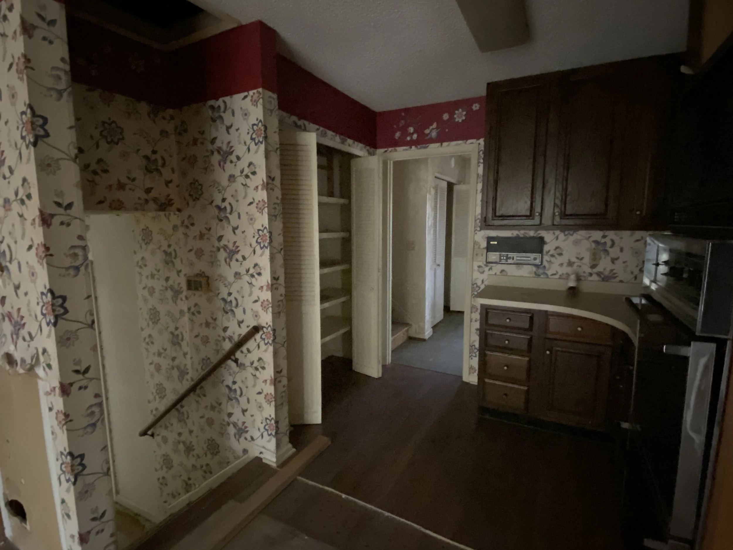 Vintage kitchen with floral wallpaper, dark wooden cabinets, and an open closet with shelves.