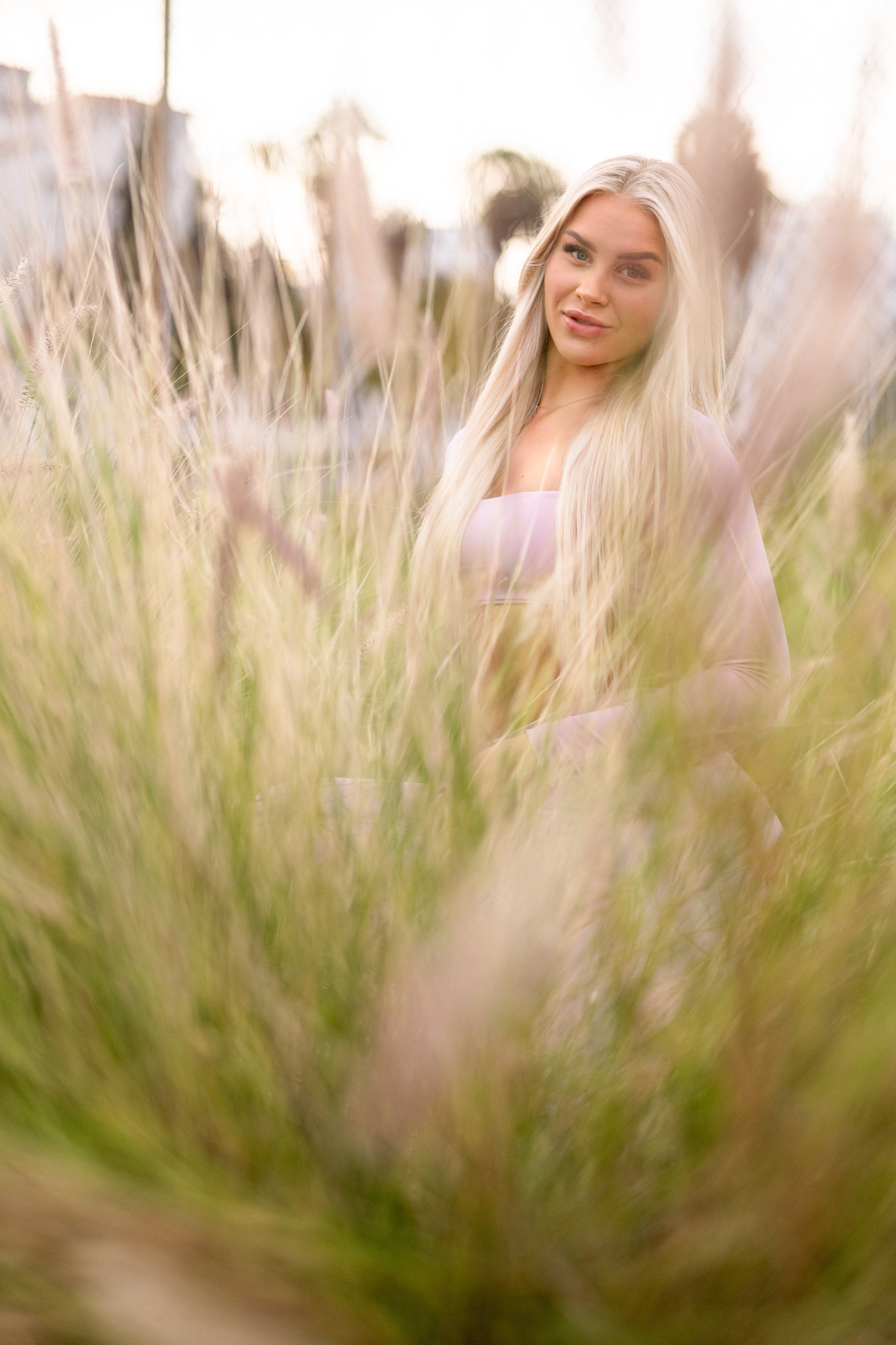 Nuori nainen seisoo niityllä pitkän hopeisen kiharaisen hiuksensa kanssa, taustalla auringonlasku ja kevyt sumu.