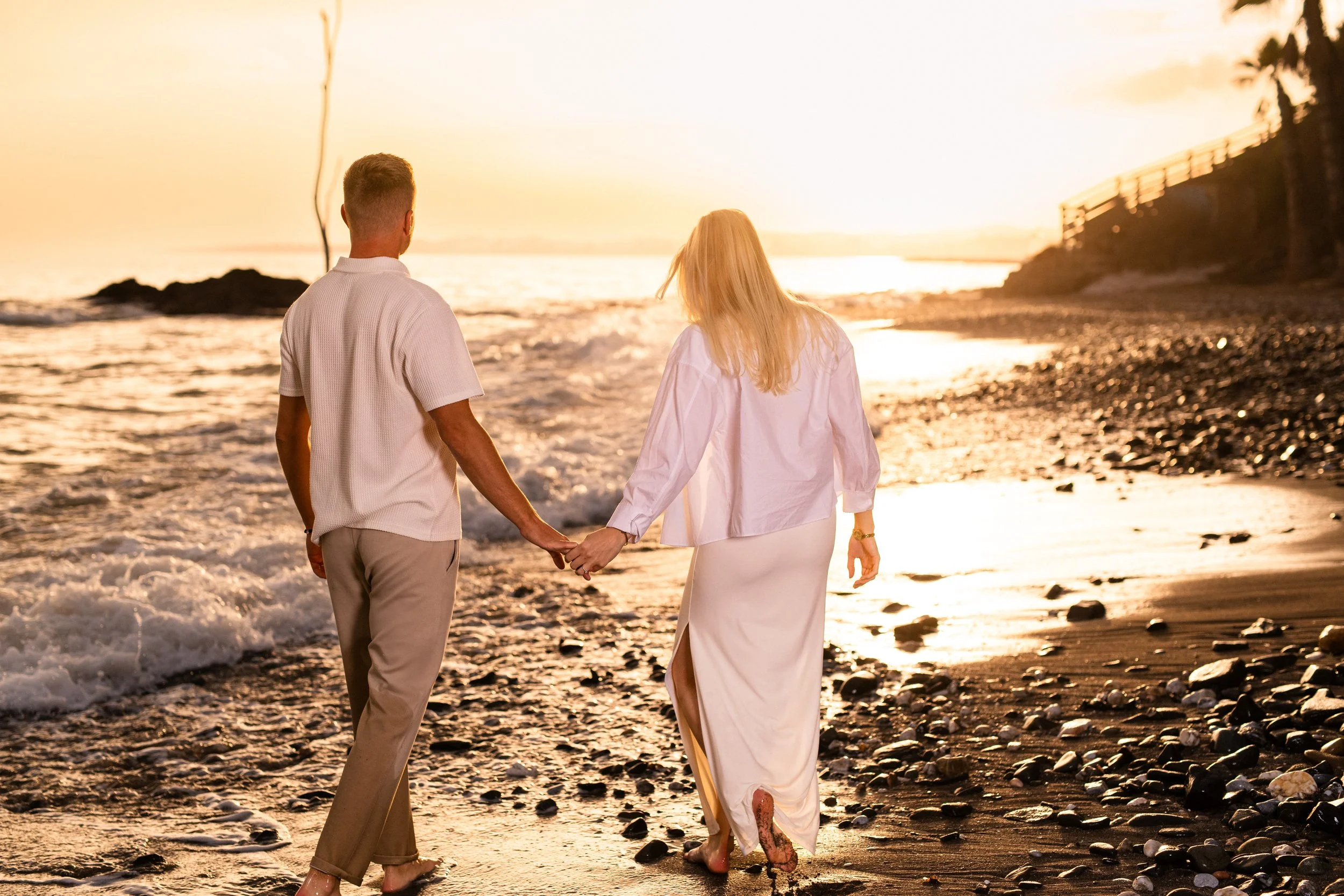 Pariskunta kävelee käsi kädessä rannalla auringonlaskun aikana.