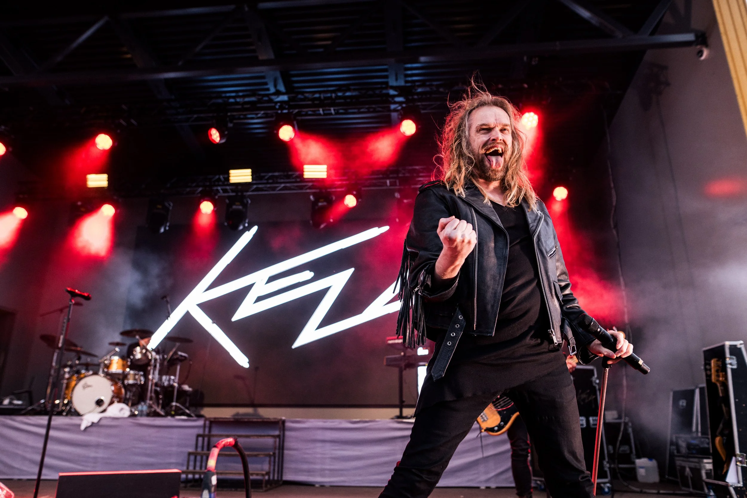 Bändi esiintyy lavalla, miehellä pitkät hiukset, musta paita ja nahkatakki.