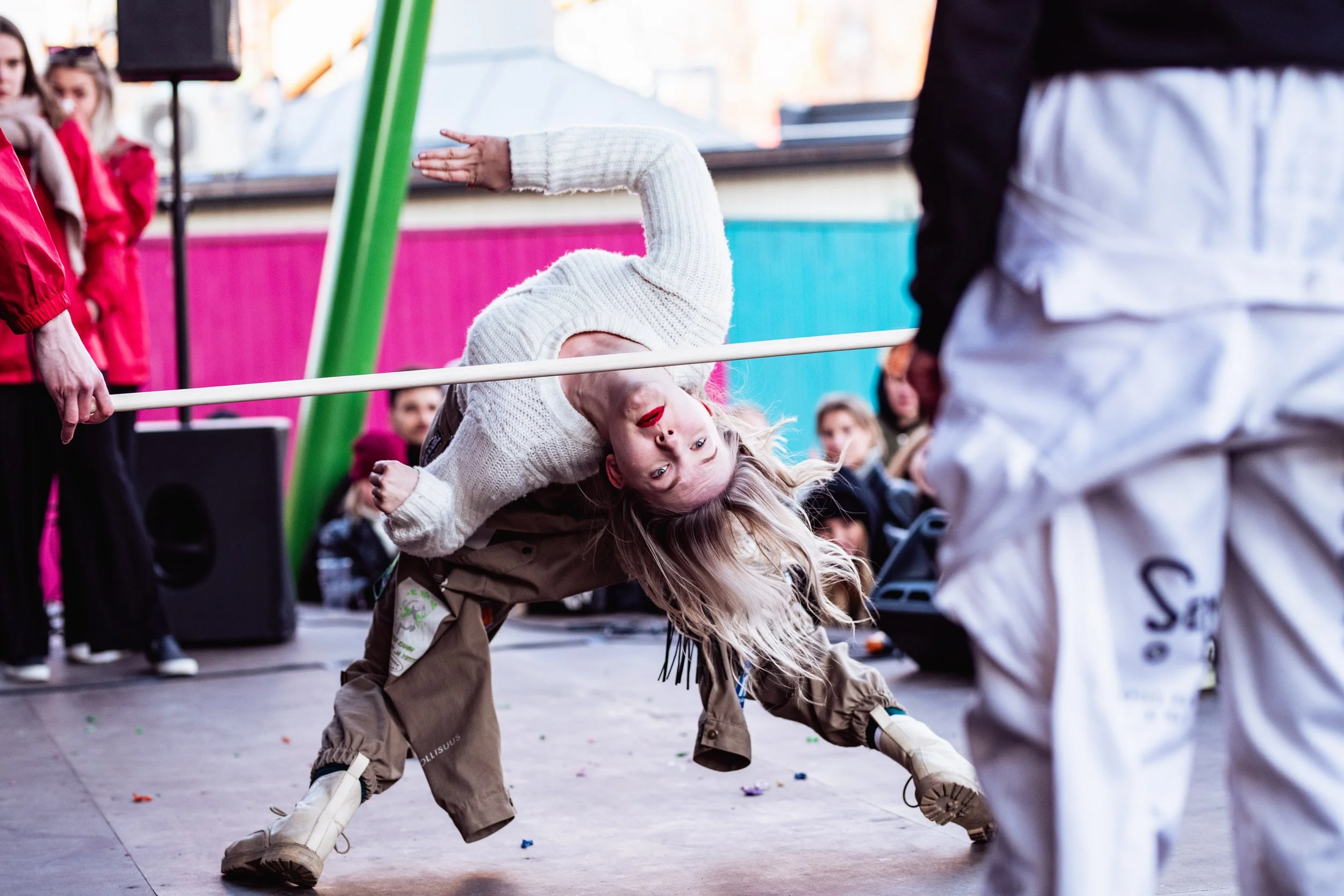 Nuori nainen taiteilee katutanssissa muiden katsellessa ja musiikkia soitetaan ulkona tapahtumassa.