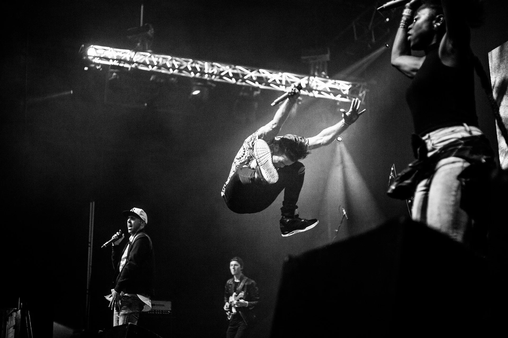 Musta-valkoinen kuva bändin esiintymisestä. Keskellä mies, joka suorastaan hyppää alas ja pitää mikrofonia kädessään. Vasemmalla toinen mies, joka myös pitää mikrofonia ja puhuu. Taustalla kitaristi, ja oikealla nainen, joka on osittain näkyvissä.