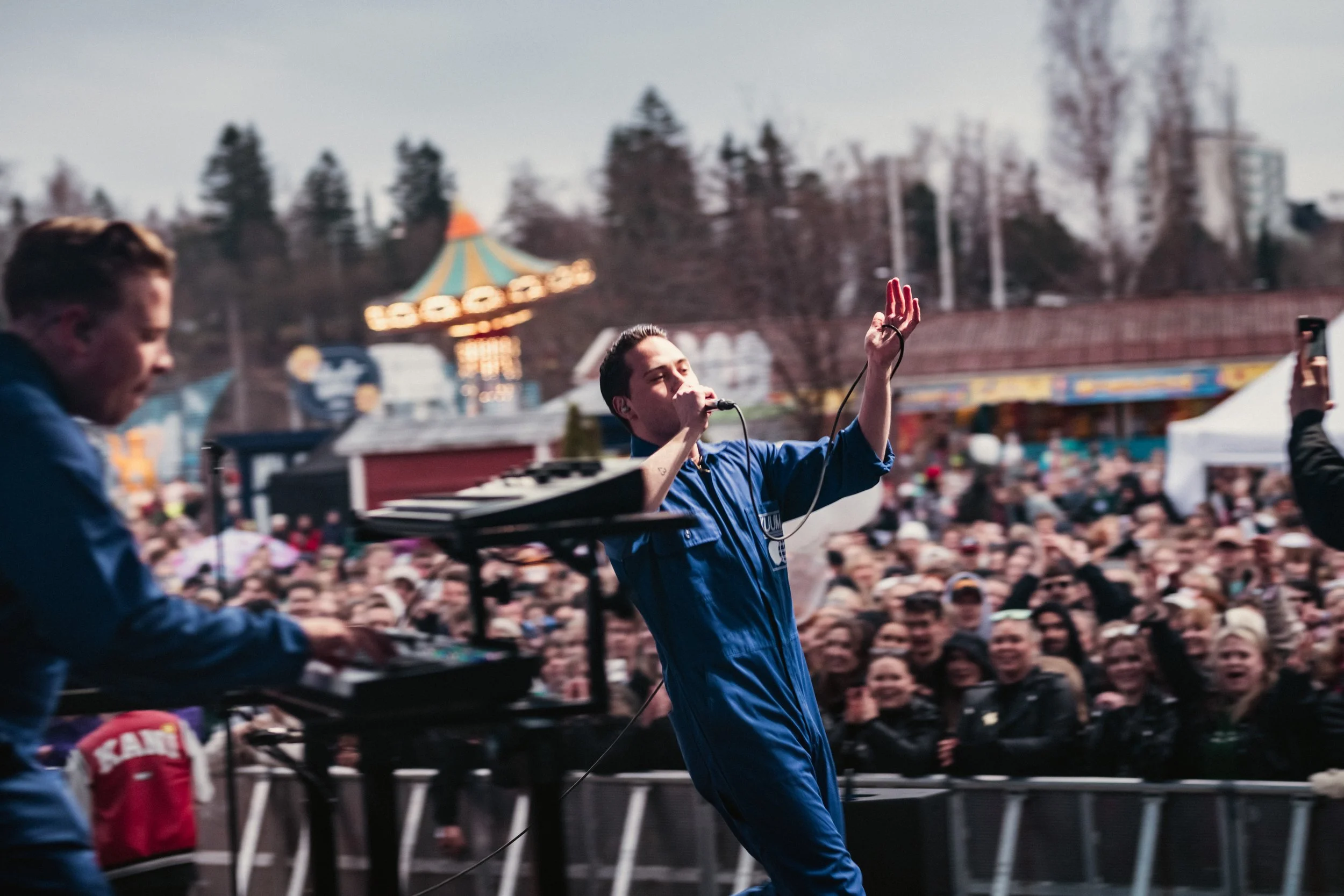 Bändi esiintyy ulkoilmakonsertissa, laulaja ja muusikko esiintymässä ja yleisö nauttimassa.