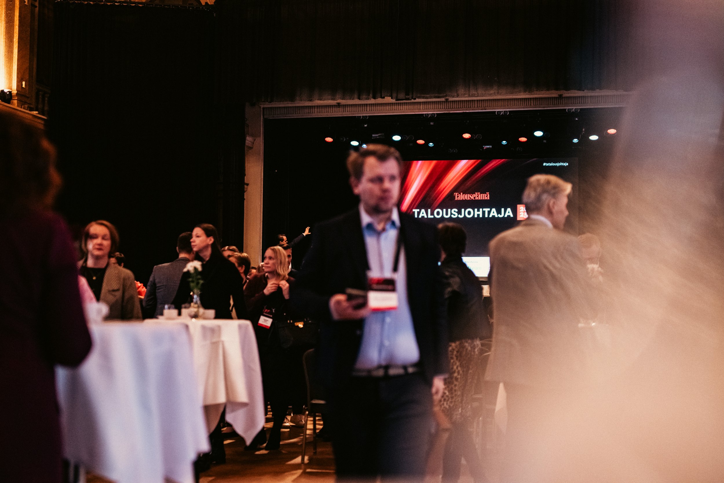 Tapahtuma, jossa ihmisiä verkostoituvat ja keskustelevat salin alueella, taustalla suuri näyttöruutu, jossa lukee 'Talousjohtaja 2023'.