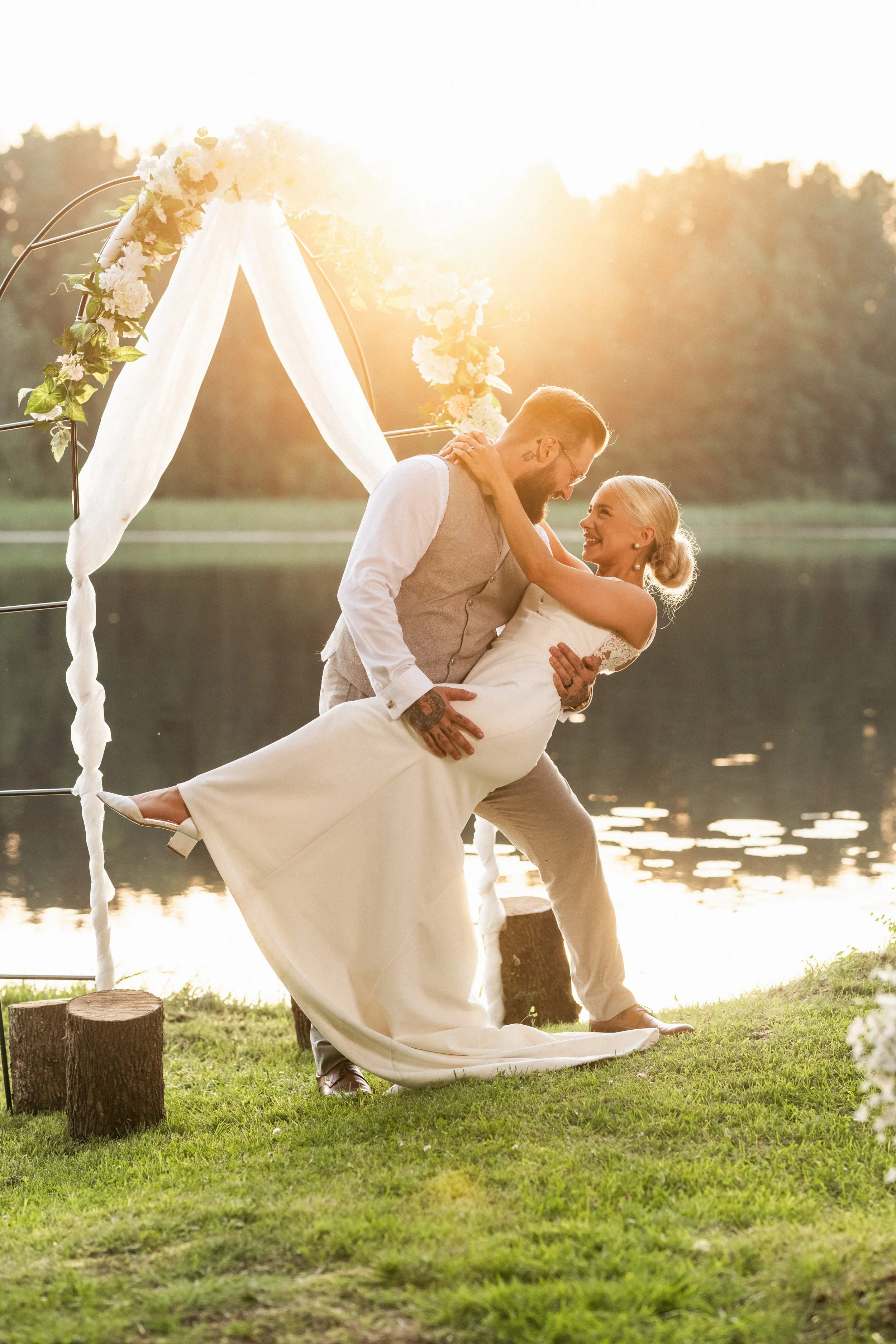 Häätanssiaiset järven rannalla auringonlaskun aikaan, pariskunta tanssimassa romanttisesti.