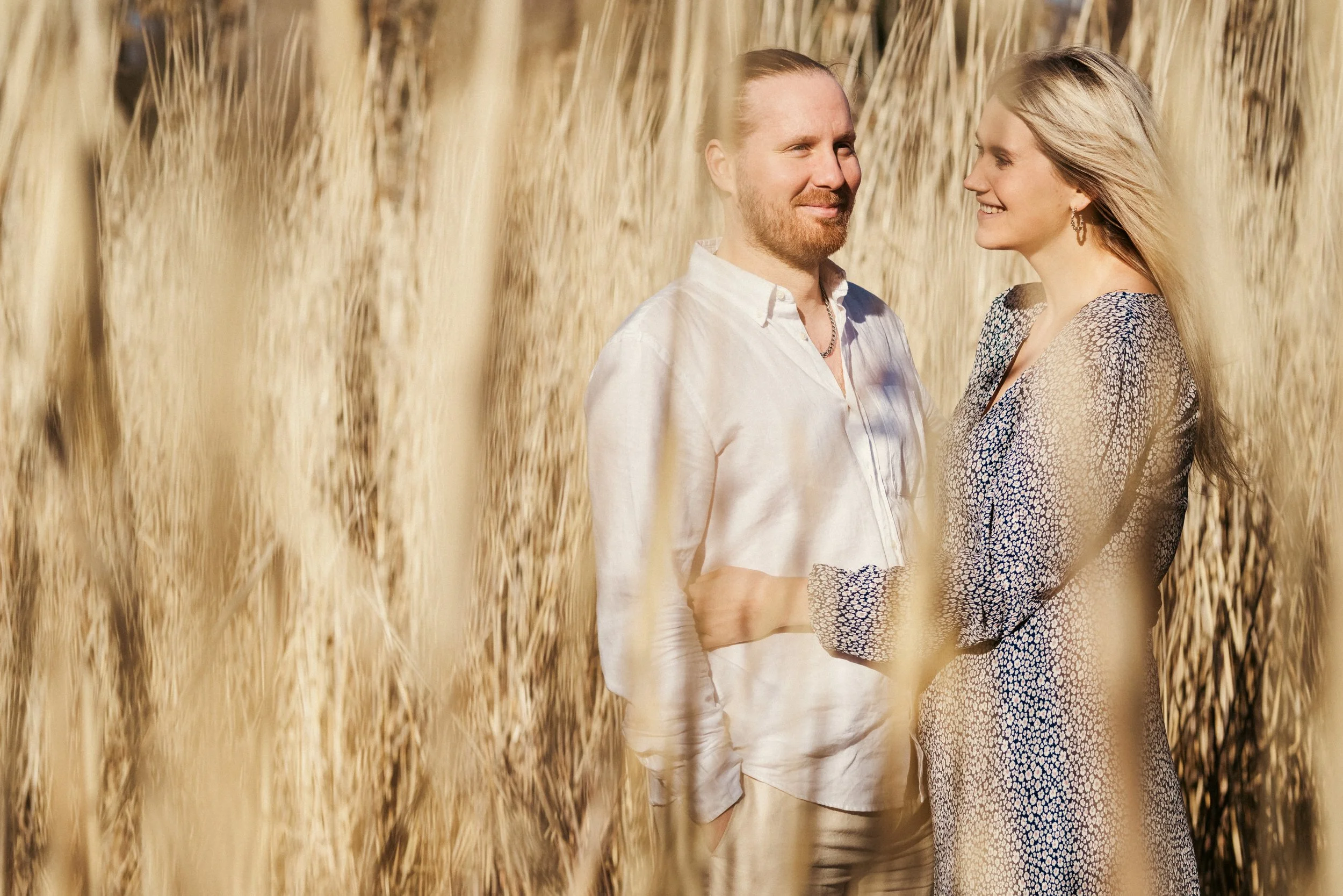 Pariskunta seisoo heinäsuovassa, katsoo toisiaan ja hymyilee.