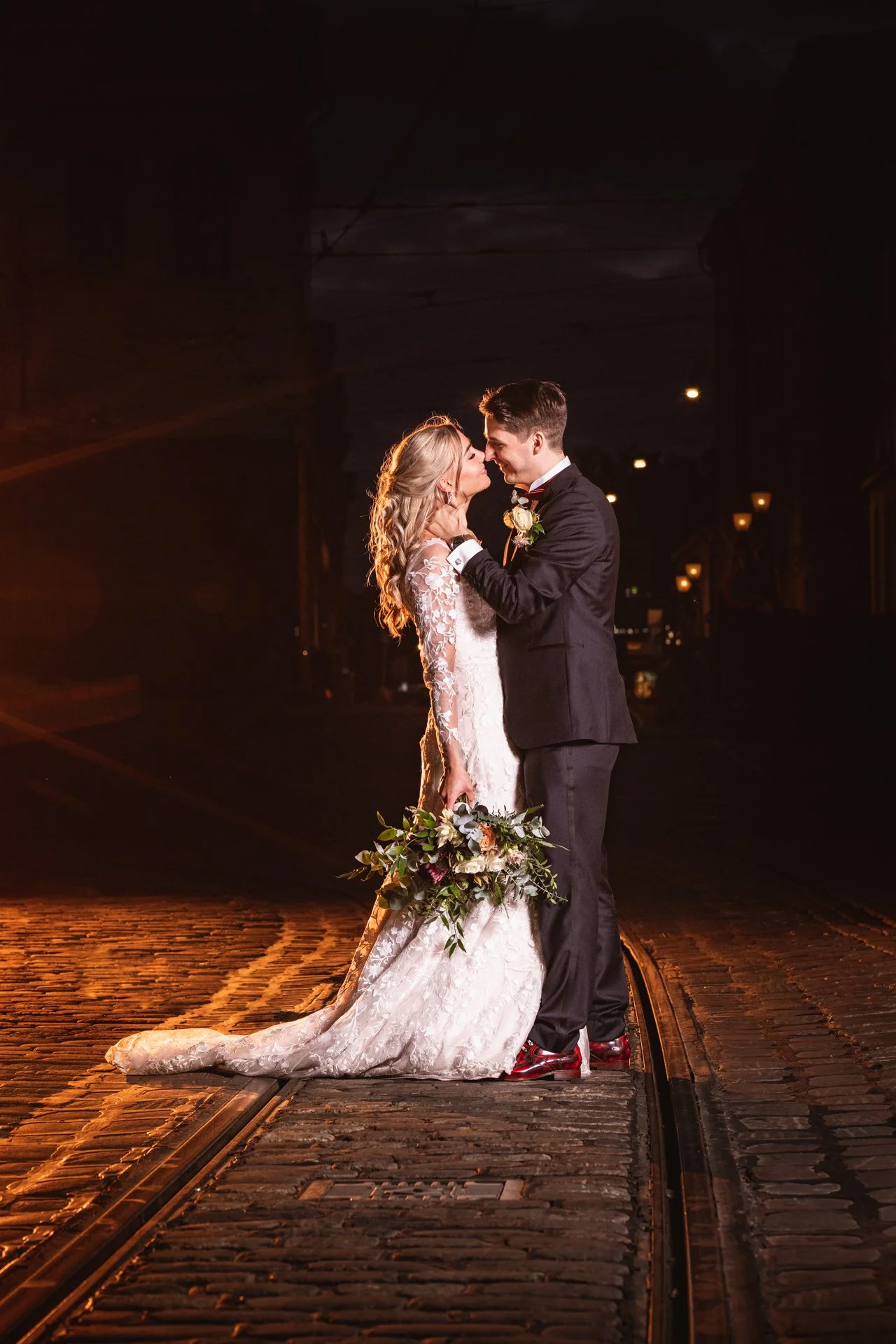 Hääpari seisoo rautatiekiskojen päällä yöllä, rakastuneina ja hymyilevät toisiaan kohti.