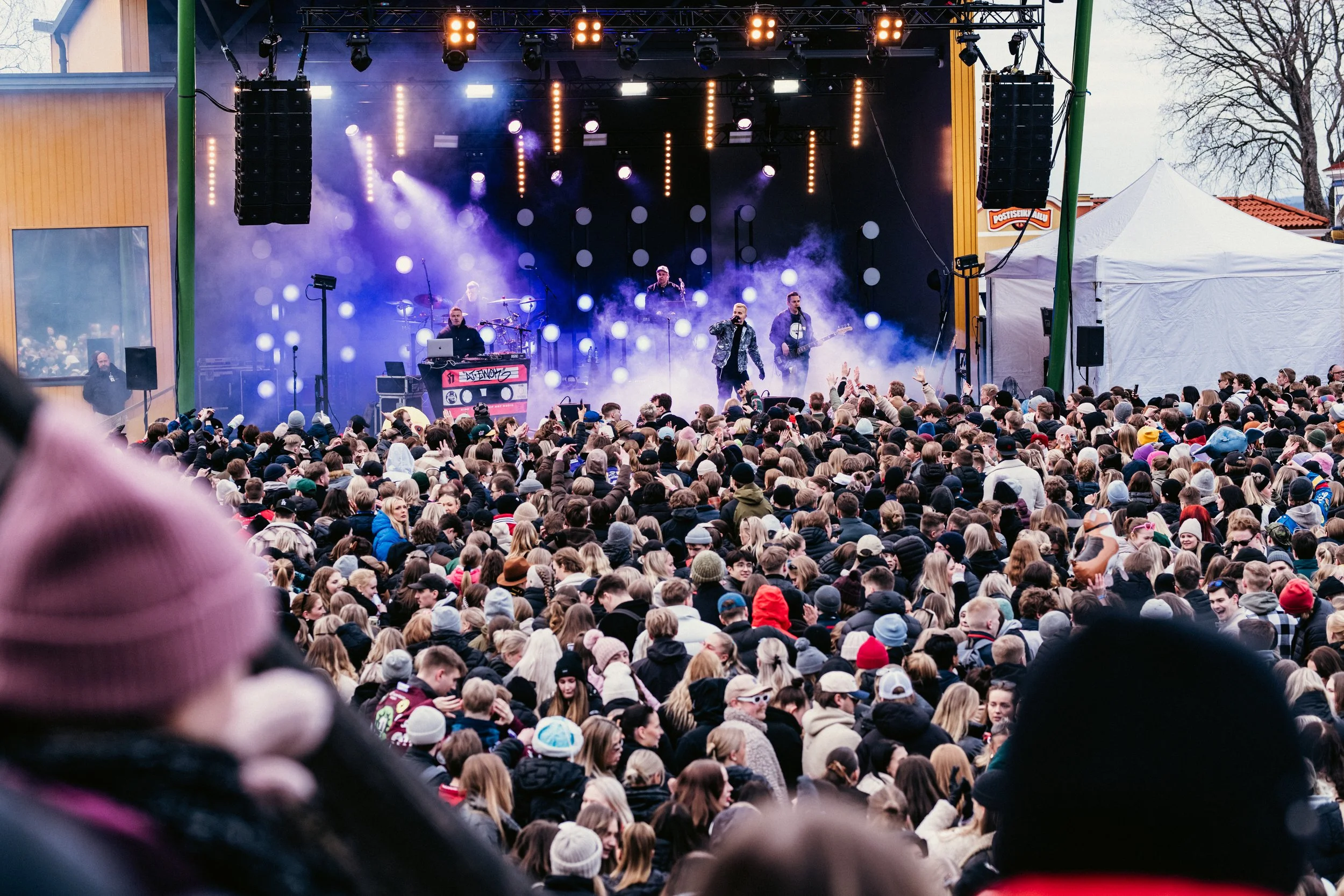 Suuri ihmisjoukko katsomassa konserttia ulkona, esiintymislavalla on bändi ja musiikkia soitetaan valojen ja savun kanssa.