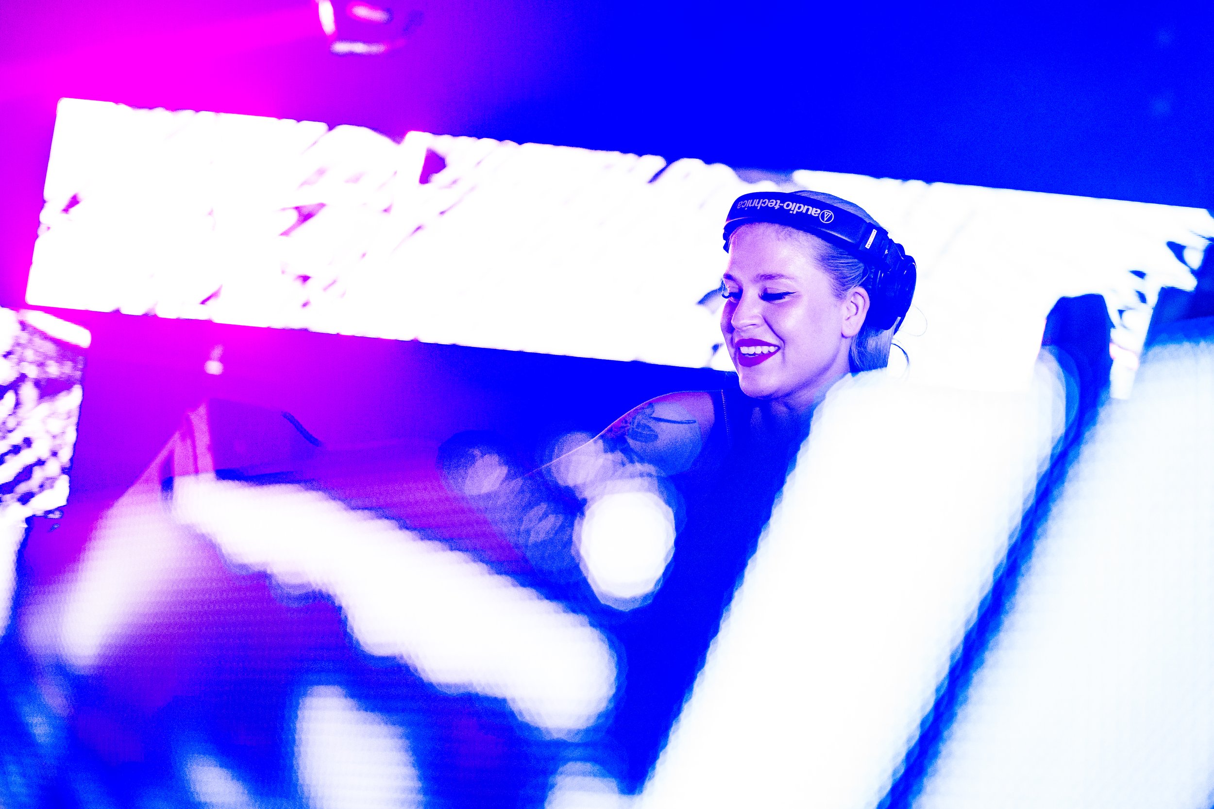 Nuori nainen, jossa on kuulokkeet, nauttii musiikista DJ-levyillä klubissa tai tapahtumassa, taustalla värikkäitä valoja.