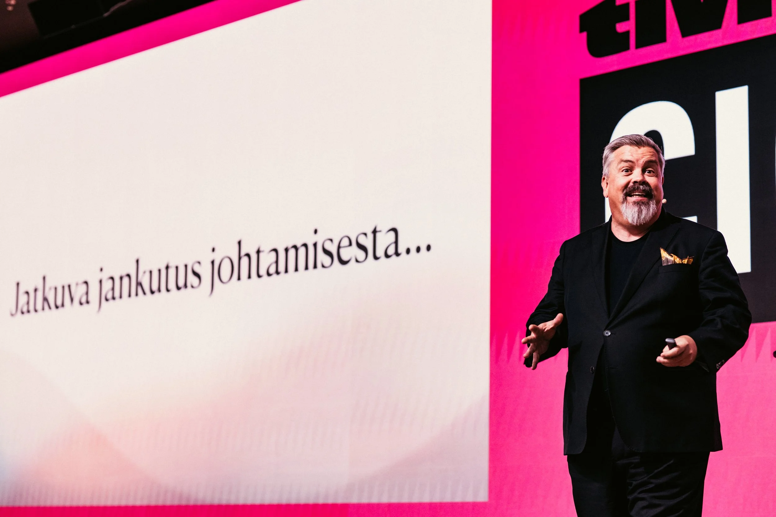 Mies puhui lavalla, taustalla suuri näyttö, jossa lukee 'Jatkuva jankutus johtamisesta...'