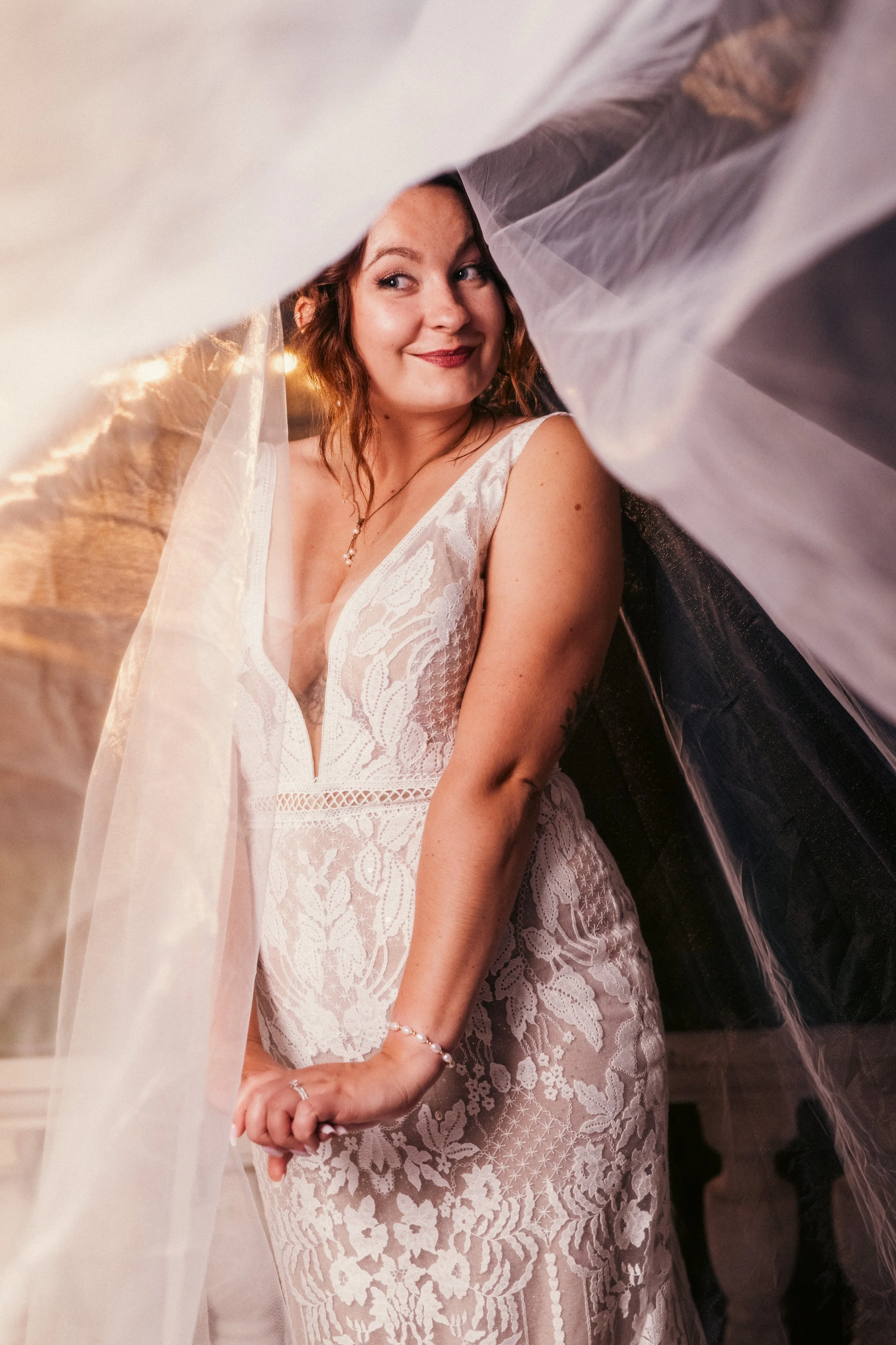 Hääpukuun pukeutunut nainen istuu korppuisen verhon takana, hymyilee ja katsoo sivulle.