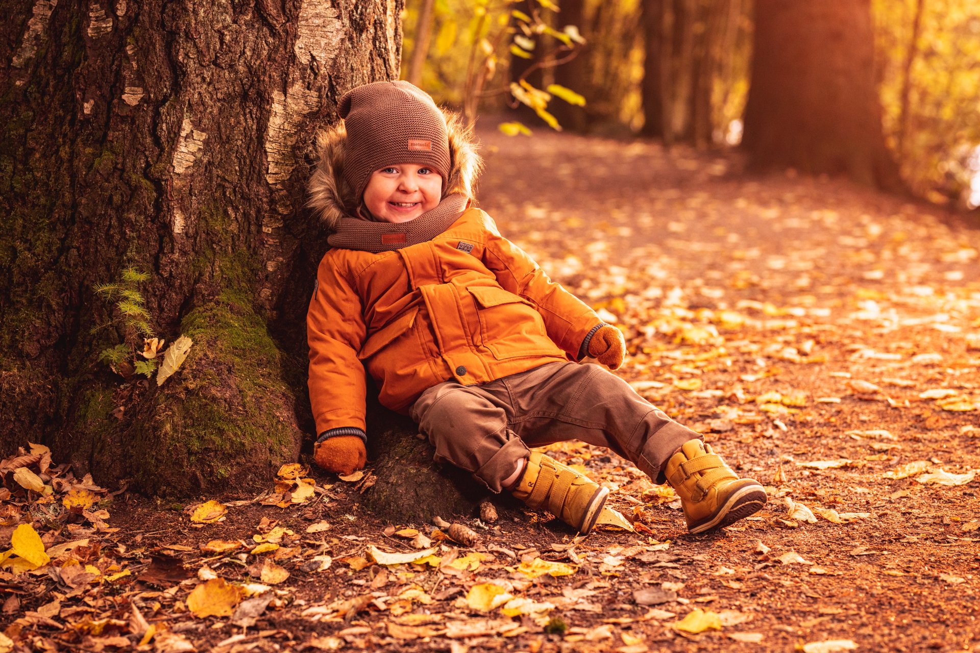 Lapsi istuu puun juurella syksyisessä metsässä.