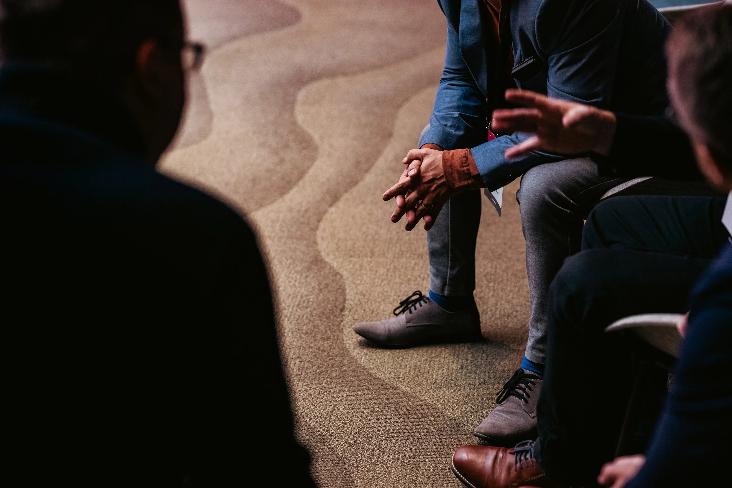 Ihmisiä istumassa keskustelutilaisuudessa, näkyvissä jalat ja kädet, keskustelu käynnissä.