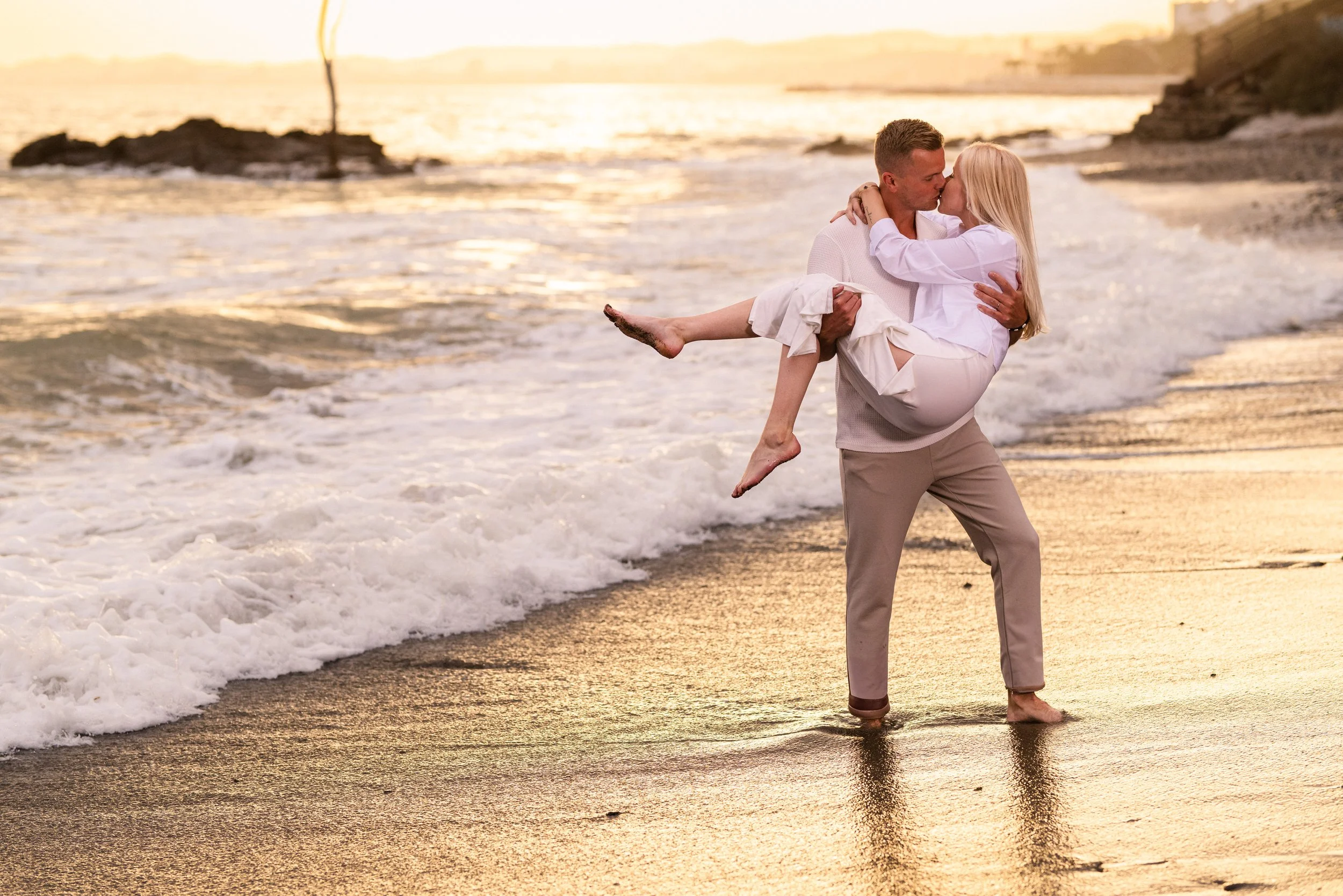 Romanttinen pariskunta kävelee rannalla auringonlaskussa, mies kantaa naista vilpittömästi.