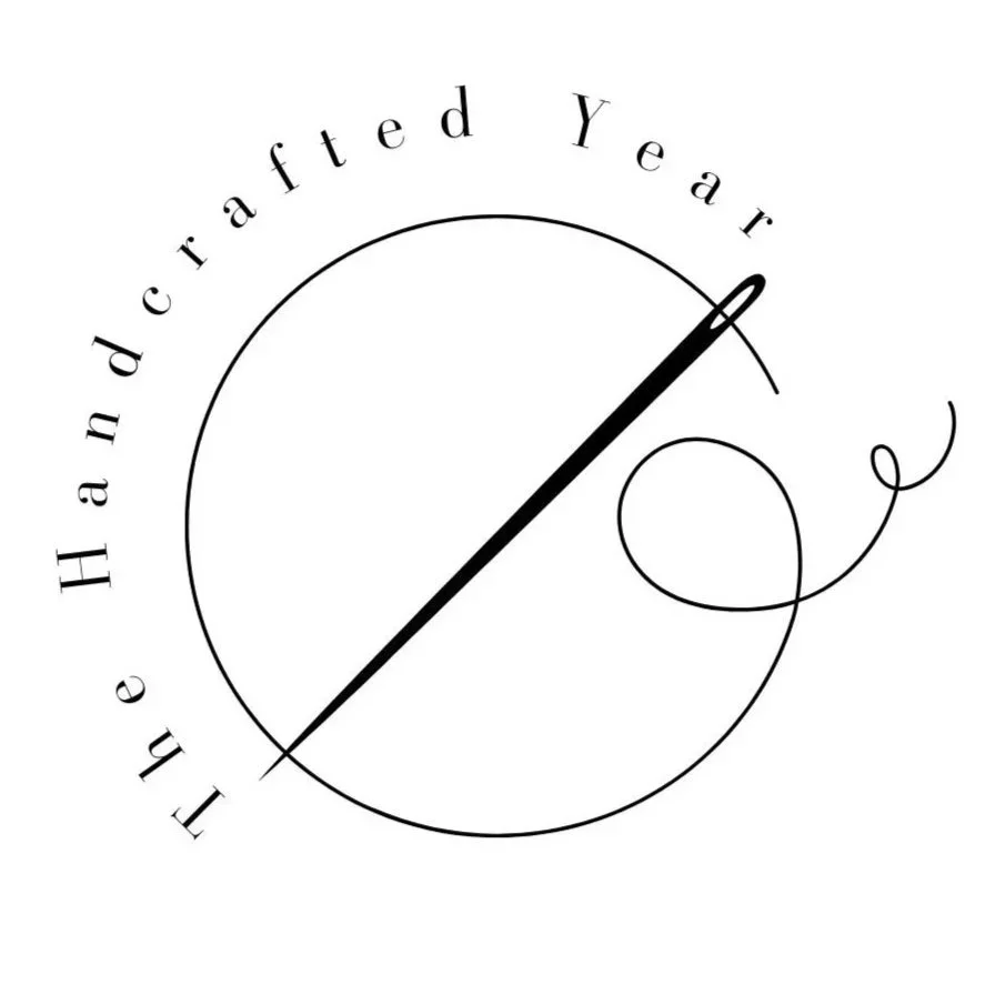 The image is a logo showing a sewing needle at an angle with a thread through its eye forming a letter 'c' the words 'The Handcrafted Year follow the curve around the c