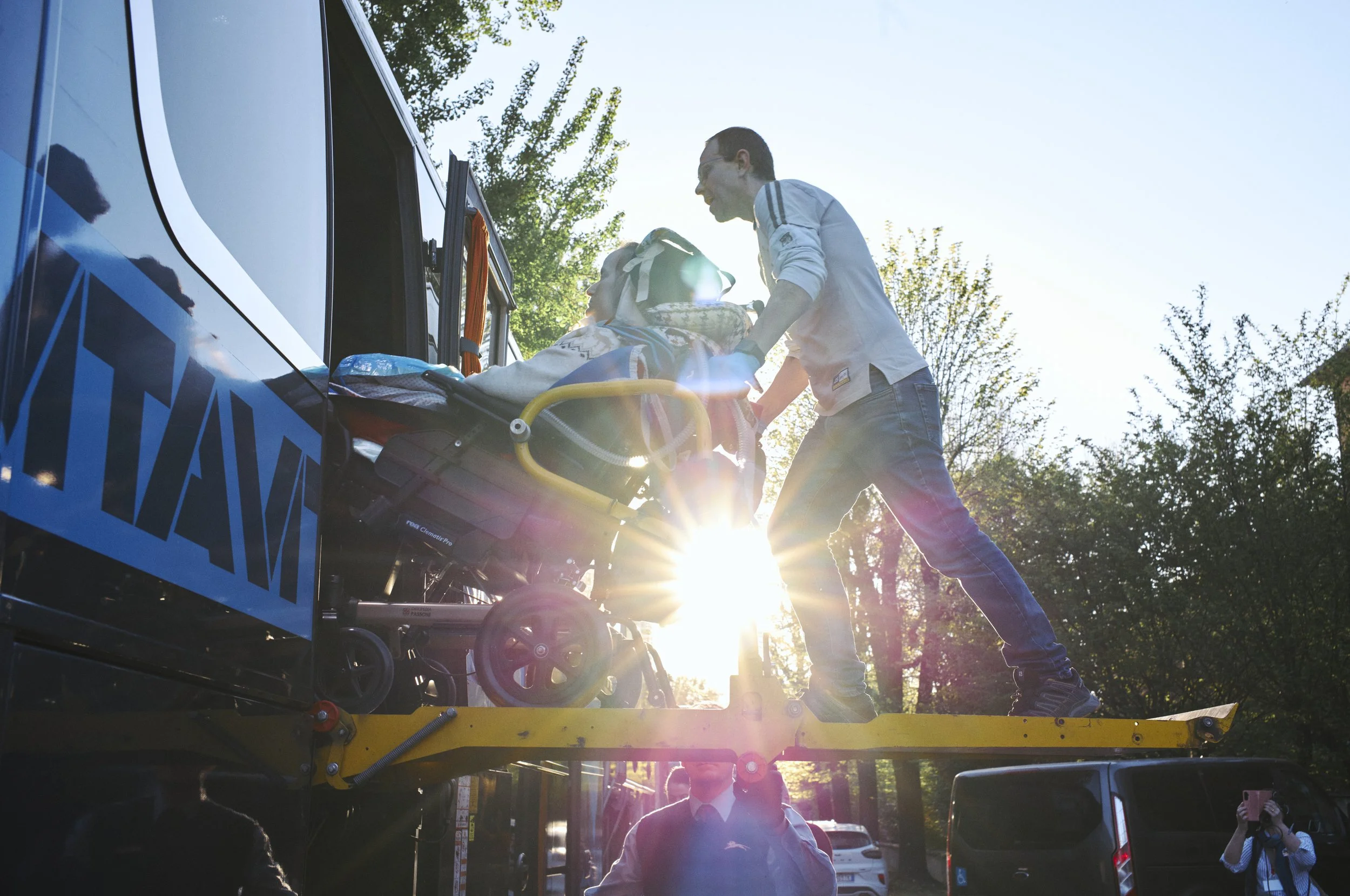 Un paramedico sta trasportando un paziente su una barella verso un'ambulanza all'aperto con il sole che splende tra gli alberi.